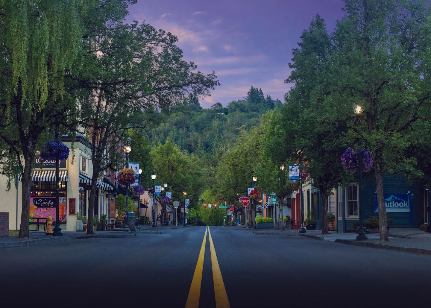 An eye-level shot looking down a paved street lined with storefronts, lush green trees, and purple twilight skies overhead.